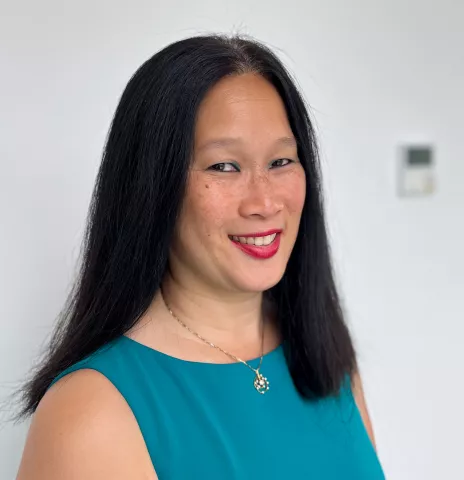 An asian woman half-smiling at the camera, wearing a teal shirt.