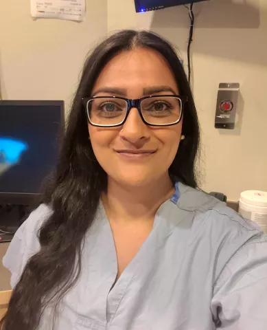 A friendly-looking south Asian woman wearing scrubs and glasses.