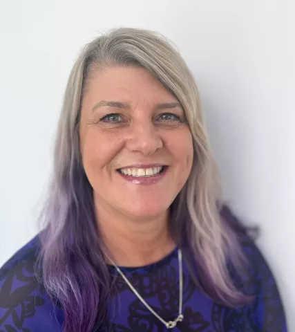 A smiling white woman with ombre blonde and purple hair and a big smile.