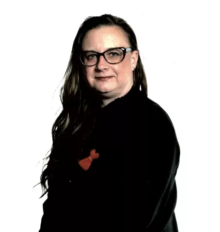 A serious looking woman with long hair, wearing black with a beaded red dress brooch.