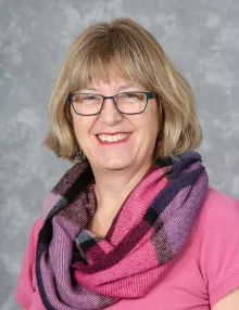 A smiling white woman, Marg Beddis, wearing shades of pink and purple.