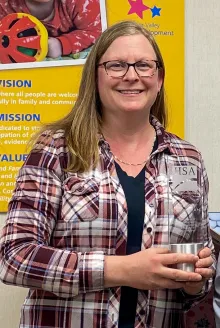 A smiling white woman with long hair, wearing a plaid flannel and holding her David Bland Award.