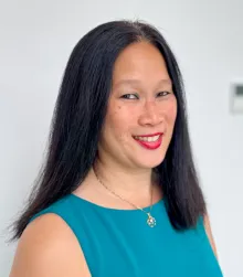 An asian woman with thick black hair wearing a teal shell and a gold necklace.