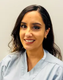 A south asian woman with long, wavy hair wearing a light blue scrub top.