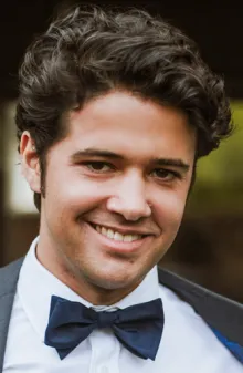 A smiling man wearing a white shirt and a black bowtie.