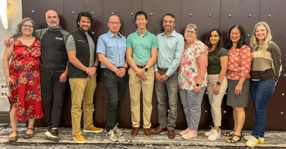 Ten health science professionals stand against the wall in a meeting room.